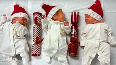 The triplets lie next to Christmas crackers