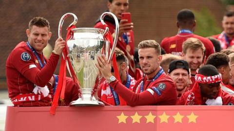 Liverpool midfielders James Milner (L) and Jordan Henderson hold the trophy on the bus