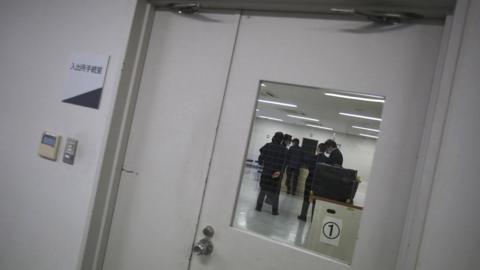 Guards seen through the window of a door at the East Japan Immigration Centre