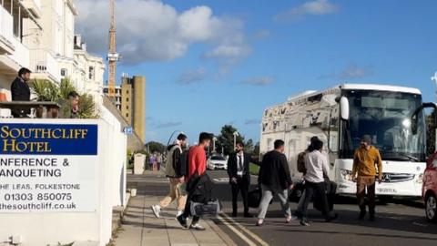 Asylum seekers boarding a bus outside a hotel in Folkestone