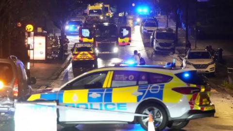 Police cars and fire engines behind a police cordon
