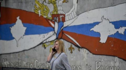 A woman walks past a mural reading "Kosovo is Serbia and Crimea is Russia" in the Serb majority north of Mitrovica, Kosovo