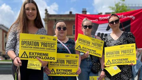 Four women holding yellow signs
