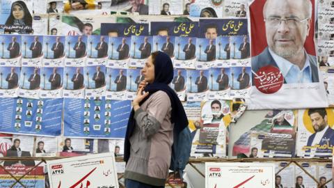 File photo showing a woman walking past electoral posters in Tehran, Iran (28 February 2024)