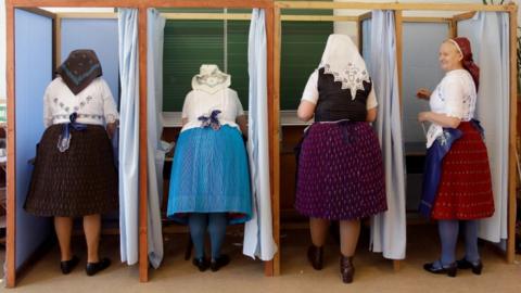 Women in traditional Hungarian outfits inside of booting booths in a school in Veresegyhaz