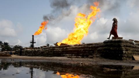 File photo: A woman walks near two gas flaring furnaces at a flow station in Ughelli, Delta State, Nigeria