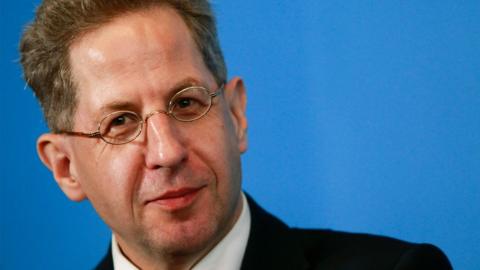 Hans-Georg Maassen looks on during a press conference, surrounded by a bright blue background