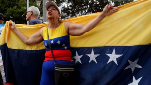 An opposition demonstrator holding a Venezuelan flag behind her back in Caracas