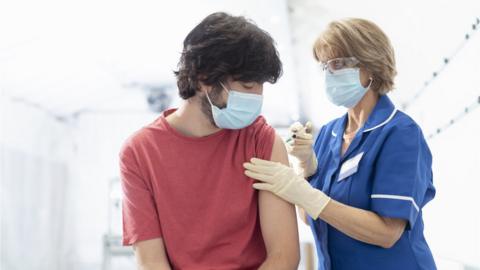 Nurse giving young man Covid-19 vaccination - stock photo