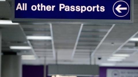 Airport sign reading 'all other passports' with a directional arrow, with passengers in the background