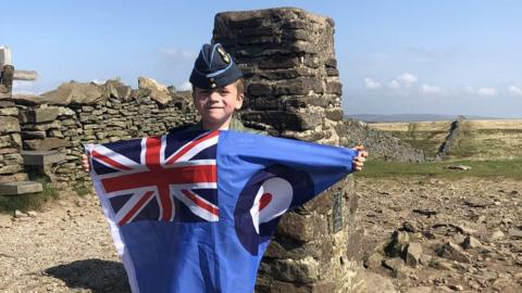 Jacob Newson waving a flag on the top of Pen-y-Ghent