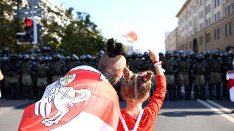 Two protesters look towards riot police in Minsk, Belarus