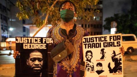 An activist holds placards in Accra, Ghana on June 6, 2020 during a protest against the death of George Floyd, an unarmed black man who died after a police officer knelt on his neck for nearly nine minutes during an arrest in Minneapolis, USA.