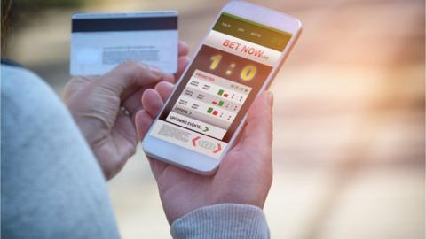 Man betting on sports, holding smart phone with working online betting mobile application