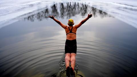 Woman diving into a pool cut into a frozen lake