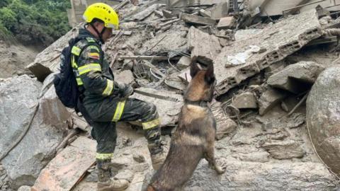 Colombia National Police rescue officer searches for victims with the help of a sniffer dog at an area damaged by a landslide which left several casualties and other injured, in Quetame, Colombia, in this photo distributed on July 18, 2023.