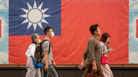 People walk next to a Taiwanese flag, in Taipei, Taiwan, 06 April 2023