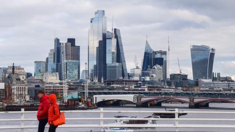 People walk along Waterloo Bridge past the City of London skyline, the capital's financial district, in January 2023