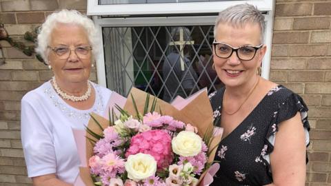 Marian Thomas and Michelle Teale jointly holding a bouquet of flowers together