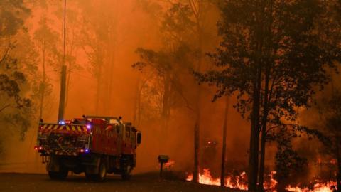 A fire truck near a raging fire in Werombi, south-west of Sydney, against a bright orange sky