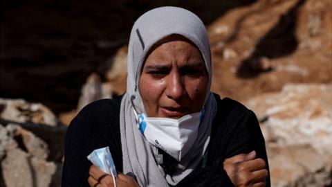 Sabrine Ferhat Bellil, who said she lost her brother, his wife and 5 of his children when the deadly storm hit her city, reacts as she stands amid rubble beside her brother's destroyed house, where she is hoping to find their bodies to bury, in Derna