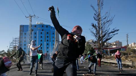 man with arm in air as if he has just thrown a stone, with many other people behind him