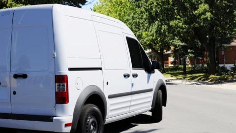 A stock image shows a stereotypical white van turning a corner on to a quiet residential street