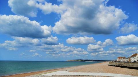 Bright blue sky with large white clouds over a greeny-blue sea and a beach in the foreground