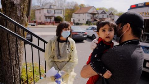 Syed Kamal holds his one year-old daughter Fareeha outside their home as Boston Medical Center pediatrician Dr. Sara Stulac does a routine check-up in an effort to use an ambulance to bring routine care and scheduled vaccinations to children amid the coronavirus disease (COVID-19) outbreak in Boston, Massachusetts, U.S., 8 May 2020