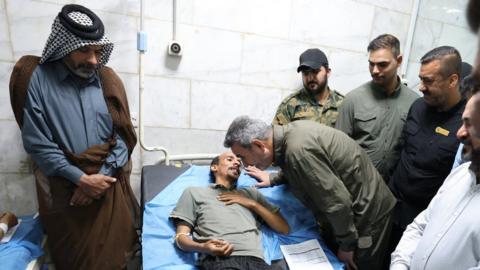 PMF chief of staff Abu Fadak Al-Mohammedawi (L) visits a man wounded in the explosion at a hospital