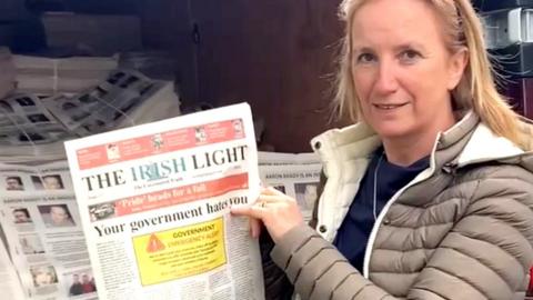 A screengrab of a video showing Gemma O'Doherty wearing a padded jacket as she displays her newspaper from the back of a van