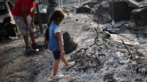 A little girl looks at a burnt bicycle in Phoenix, Oregon