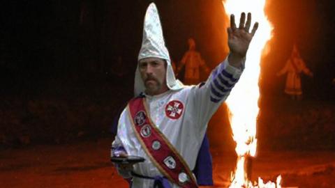 Frank Ancona, wearing a white hood and standing in front of a burning cross