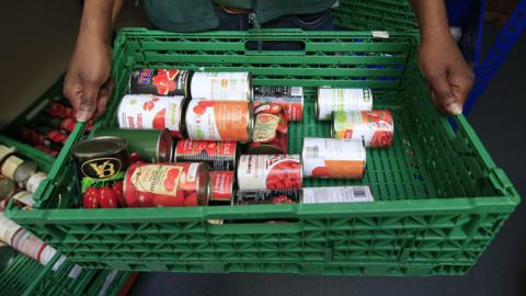 A foodbank worker holding a basket of tinned food
