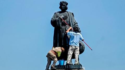 Municipal workers clean a statue of Christopher Columbus, which was protected by a metal fence after activists called to tear it down on social networks, in Mexico City, on October 12, 2020.