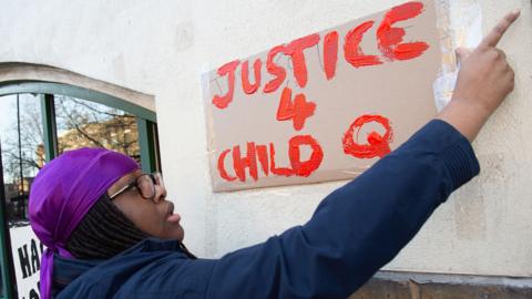 A woman hangs a placard on the wall outside Stoke Newington police station during the demonstration.