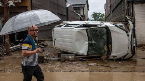 A man walks past an overnturned car