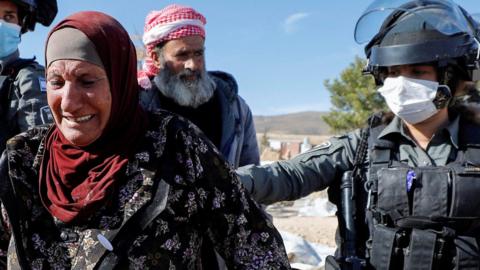 A Palestinian woman, accompanied by Israeli forces, reacts as a building is demolished in Yatta, in the Israeli-occupied West Bank (12 January 2022)