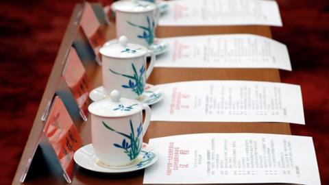 Cups of tea and agendas lined up on a table.