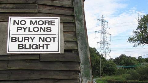 Pylons in East Anglia in the background to a protest sign on the side of a wooden barn.