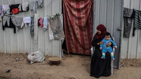 A woman holds a child while sitting outside a shelter in Gaza
