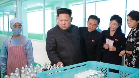 Kim Jong Un holds clear liquid samples in bottles at factory visit