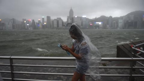 A woman uses her phone while wearing a plastic poncho along Victoria Harbour during heavy winds and rain brought on by Typhoon Hato in Hong Kong on 23 August 2017.