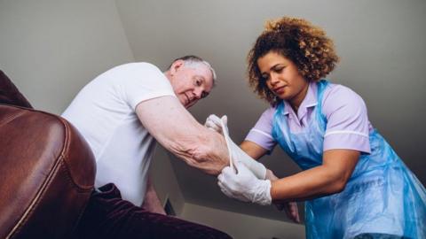 Nurse in blue plastic apron puts a bandage on an older man's arm