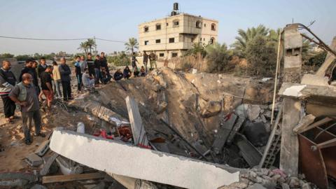 Palestinians gather around the remains of a building destroyed in an Israeli air strike in the southern Gaza Strip (13 November 2019)