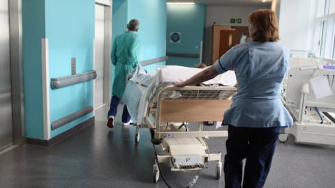 Staff pushing a bed through a hospital