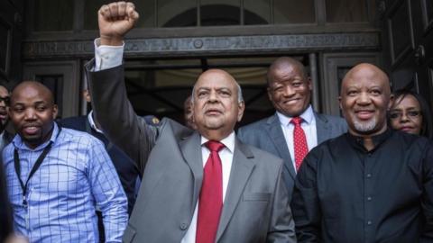 Former South African Finance Minister Pravin Gordhan raises his fist as he addresses a group of supporters outside the South African National Treasury in Pretoria