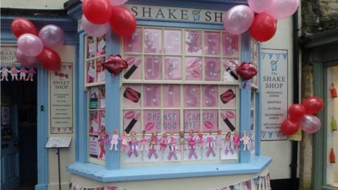 A shop with loads of pink balloons and pink signs in the window.