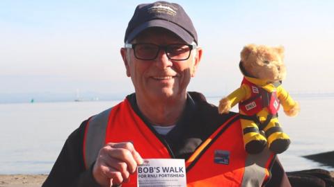 Bob Crane holding a leaflet about his fundraising challenge. He has a teddy bear, named Captain Flint, on his shoulder