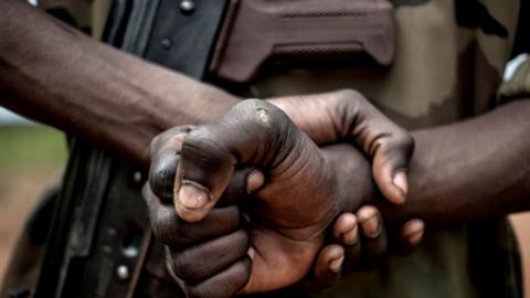 A man carrying a gun and clenching his fists.